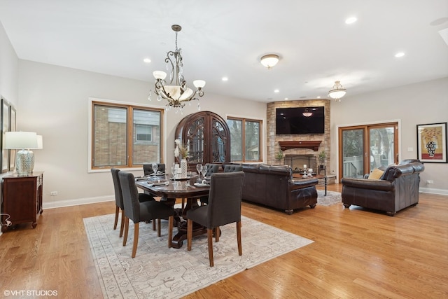 dining space featuring a stone fireplace, light wood-type flooring, and an inviting chandelier