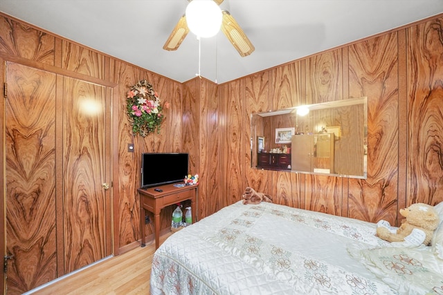 bedroom with ceiling fan, wooden walls, and hardwood / wood-style floors