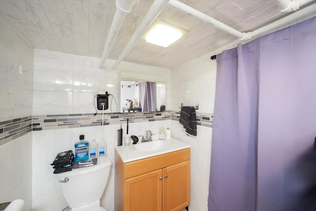 bathroom featuring toilet, curtained shower, vanity, and tile walls