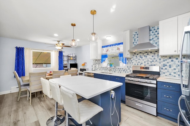 kitchen featuring appliances with stainless steel finishes, blue cabinets, hanging light fixtures, white cabinetry, and wall chimney exhaust hood