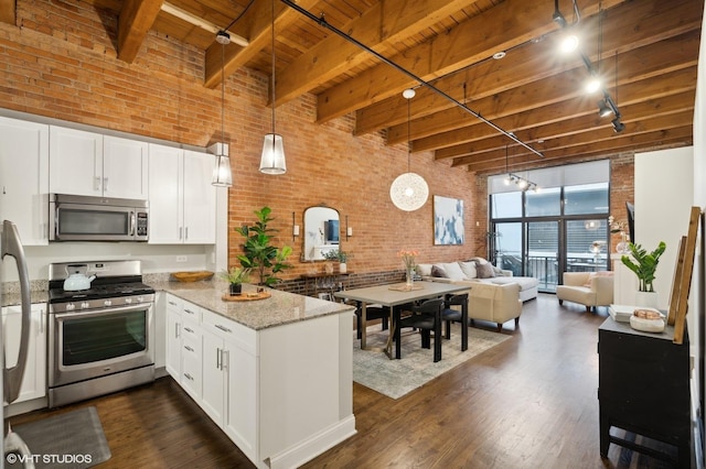 kitchen with brick wall, stainless steel appliances, pendant lighting, and white cabinets