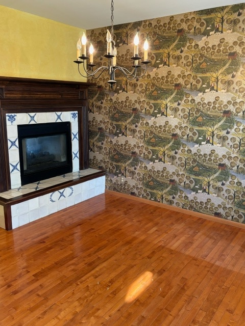 unfurnished living room featuring wood-type flooring, a tile fireplace, and an inviting chandelier