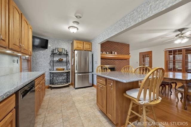 kitchen featuring appliances with stainless steel finishes, a brick fireplace, ceiling fan, a kitchen island, and a breakfast bar area