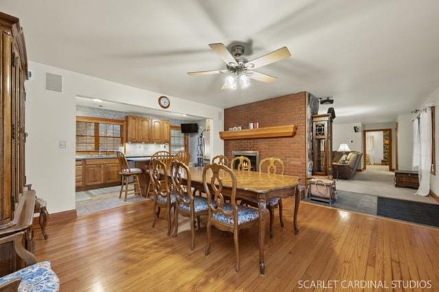 dining room featuring light wood-type flooring, a brick fireplace, and ceiling fan