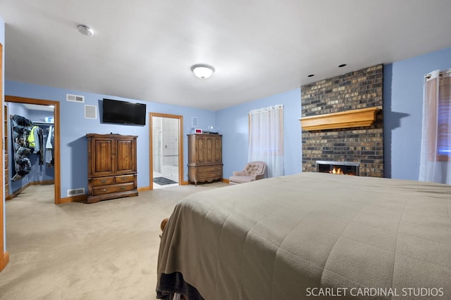 bedroom with ensuite bath, a fireplace, light colored carpet, a walk in closet, and a closet