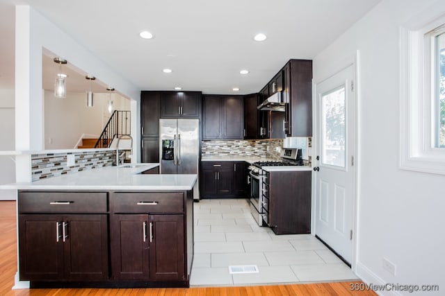 kitchen with dark brown cabinetry, light hardwood / wood-style floors, appliances with stainless steel finishes, decorative light fixtures, and backsplash