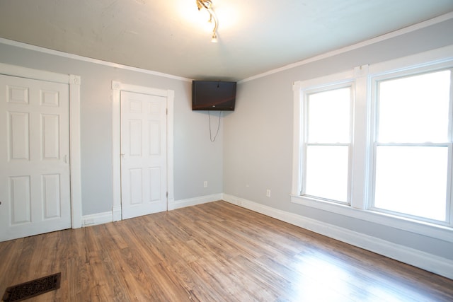 unfurnished bedroom featuring ornamental molding, multiple windows, and wood-type flooring