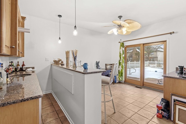 kitchen featuring dark stone countertops, light tile patterned floors, decorative light fixtures, kitchen peninsula, and a breakfast bar area