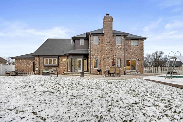 snow covered back of property featuring a patio