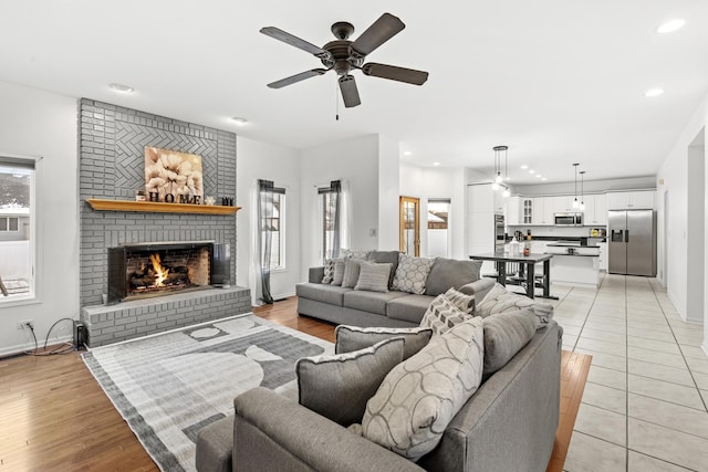 living room with light hardwood / wood-style floors, a brick fireplace, ceiling fan, and a healthy amount of sunlight