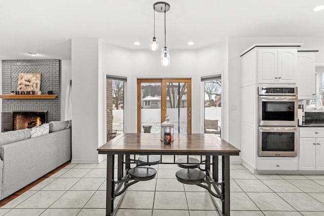 kitchen featuring white cabinetry, stainless steel double oven, pendant lighting, a fireplace, and light tile patterned floors