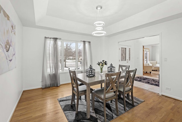 dining space featuring hardwood / wood-style floors, a notable chandelier, and a raised ceiling