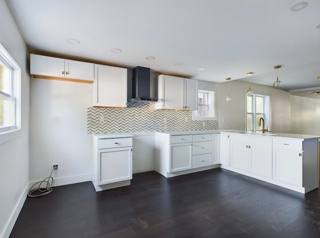 kitchen featuring wall chimney range hood, kitchen peninsula, white cabinetry, and pendant lighting