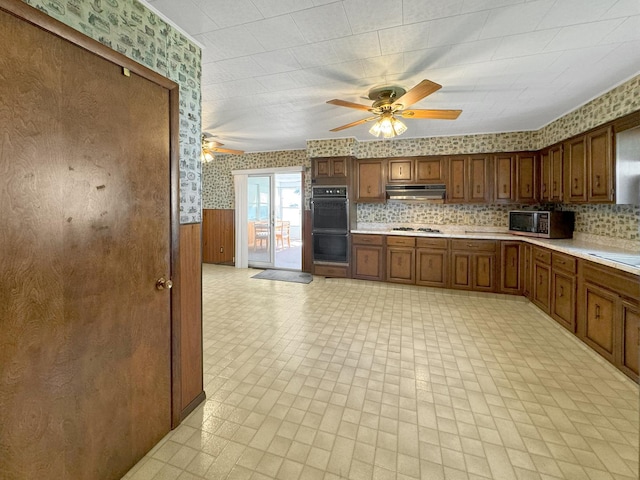 kitchen featuring wallpapered walls, under cabinet range hood, wainscoting, light countertops, and a ceiling fan
