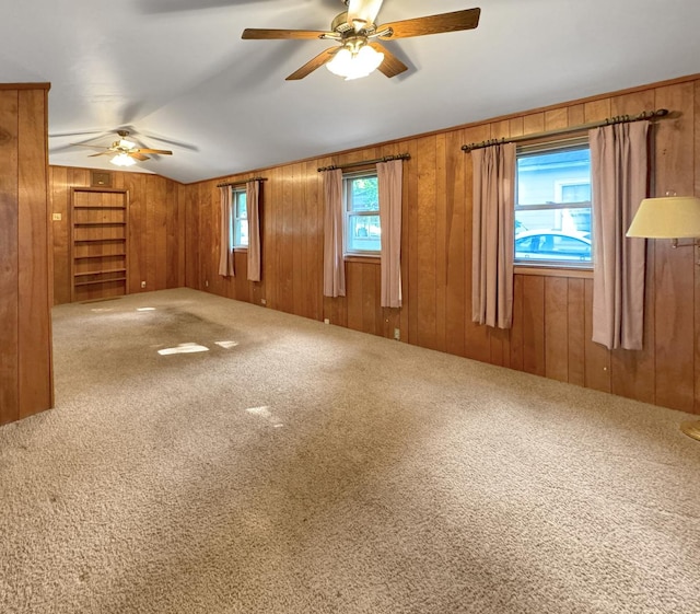 empty room with ceiling fan, carpet flooring, wooden walls, and lofted ceiling