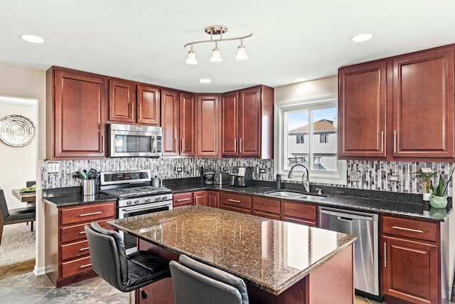 kitchen with sink, a kitchen island, stainless steel appliances, a breakfast bar, and dark stone countertops