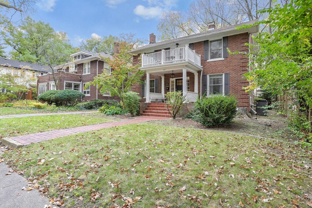 1105 S Busey Ave, Urbana, IL 61801 - colonial inspired home with covered porch, brick siding, a balcony, a front lawn, and a chimney
