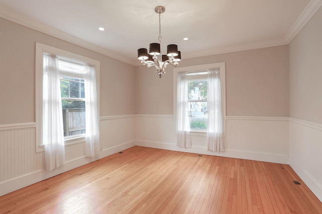 spare room featuring light hardwood / wood-style flooring, ornamental molding, a chandelier, and a wealth of natural light