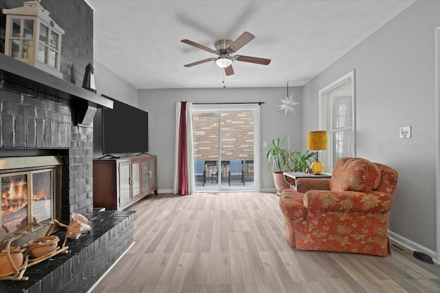 living room featuring a brick fireplace, light hardwood / wood-style flooring, and ceiling fan