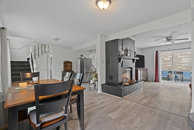 dining room with wood-type flooring, a brick fireplace, and ceiling fan