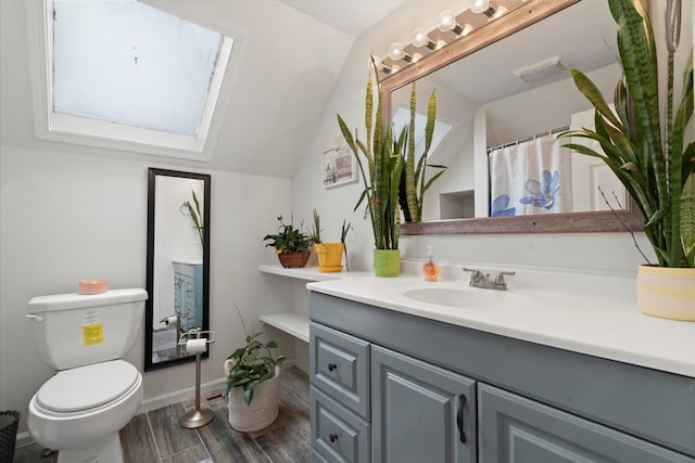 bathroom with vaulted ceiling with skylight, hardwood / wood-style floors, vanity, and toilet