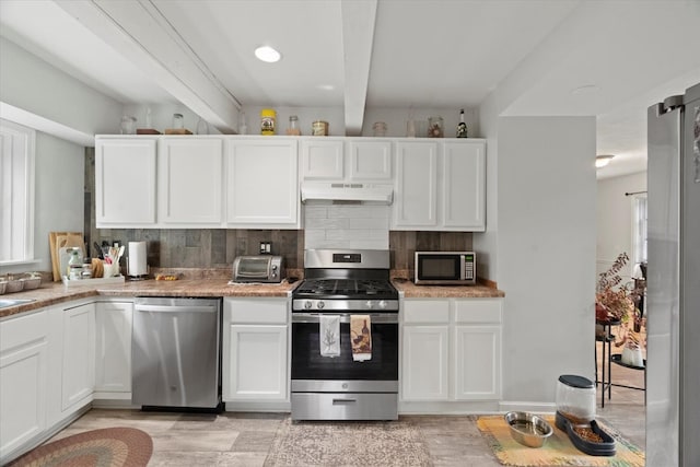 kitchen with beam ceiling, white cabinetry, appliances with stainless steel finishes, range hood, and decorative backsplash