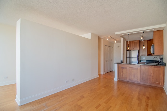 kitchen with a textured ceiling, appliances with stainless steel finishes, decorative light fixtures, and light wood-type flooring