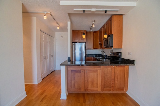 kitchen with light hardwood / wood-style floors, appliances with stainless steel finishes, a textured ceiling, and kitchen peninsula