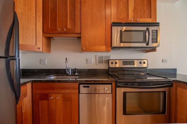 kitchen with appliances with stainless steel finishes, sink, and dark stone counters