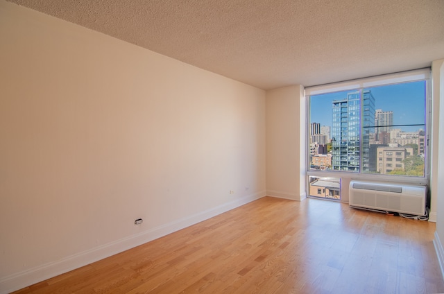 empty room with light hardwood / wood-style floors, a textured ceiling, a wall of windows, and a wall mounted AC