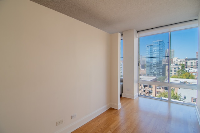 spare room featuring light hardwood / wood-style floors, a textured ceiling, and a wall of windows