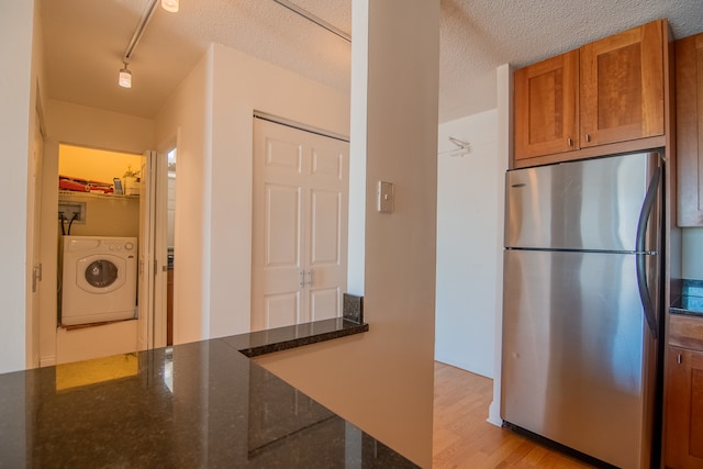 kitchen with light hardwood / wood-style floors, washer / clothes dryer, dark stone counters, and stainless steel fridge