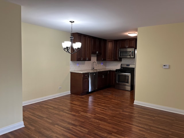 kitchen featuring backsplash, appliances with stainless steel finishes, hanging light fixtures, and dark hardwood / wood-style flooring