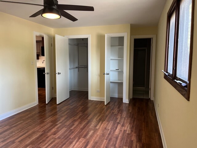 unfurnished bedroom with dark wood-type flooring, multiple closets, and ceiling fan