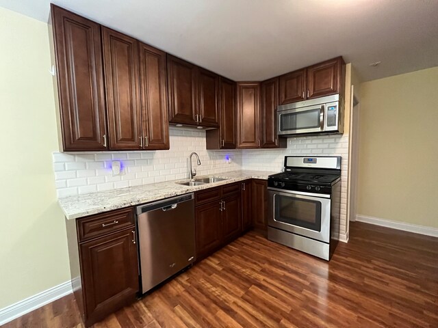 kitchen featuring sink, tasteful backsplash, appliances with stainless steel finishes, dark hardwood / wood-style floors, and light stone countertops