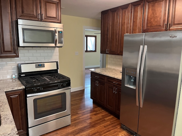 kitchen with dark wood-type flooring, light stone countertops, backsplash, and appliances with stainless steel finishes