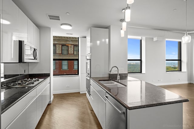 kitchen with pendant lighting, dark hardwood / wood-style flooring, a center island with sink, stainless steel appliances, and white cabinetry