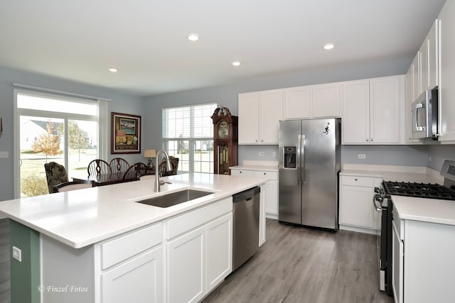 kitchen featuring stainless steel appliances, white cabinets, sink, light hardwood / wood-style floors, and a center island with sink