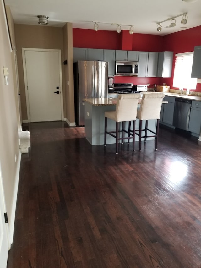 kitchen featuring gray cabinetry, a center island, dark wood-type flooring, a kitchen bar, and appliances with stainless steel finishes