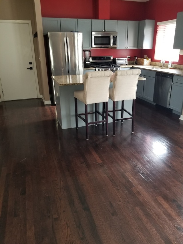 kitchen with light stone countertops, stainless steel appliances, a kitchen breakfast bar, dark hardwood / wood-style flooring, and a kitchen island