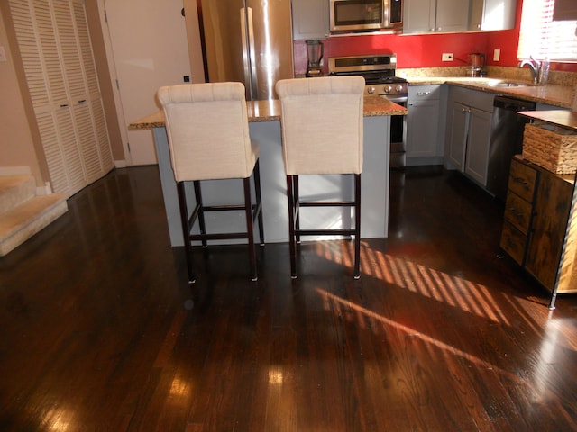 kitchen with a kitchen breakfast bar, a center island, dark wood-type flooring, and appliances with stainless steel finishes