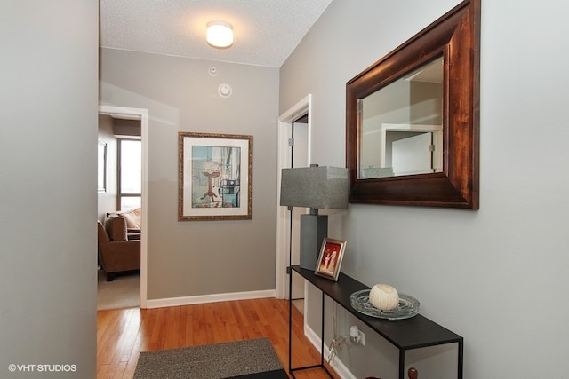 corridor featuring lofted ceiling, light hardwood / wood-style flooring, and a textured ceiling