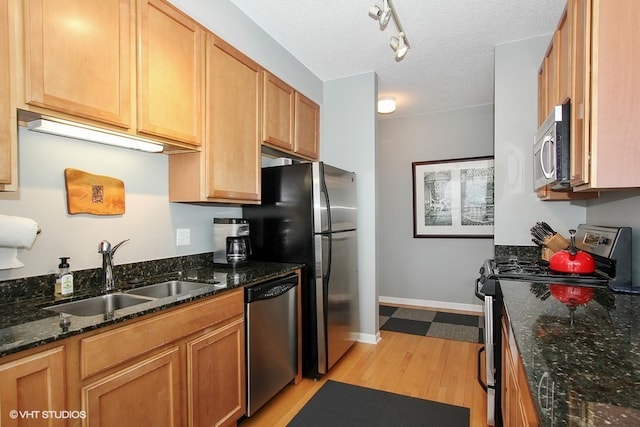 kitchen featuring sink, a textured ceiling, appliances with stainless steel finishes, dark stone countertops, and light wood-type flooring