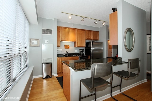 kitchen featuring dark stone countertops, stainless steel refrigerator, light hardwood / wood-style flooring, a kitchen breakfast bar, and a textured ceiling