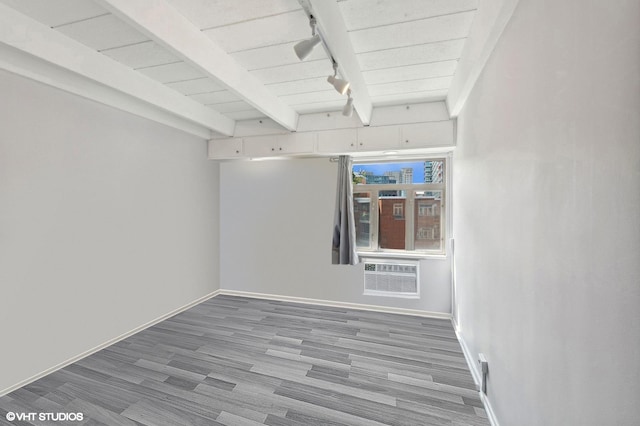 spare room with a wall unit AC, beam ceiling, track lighting, and light wood-type flooring