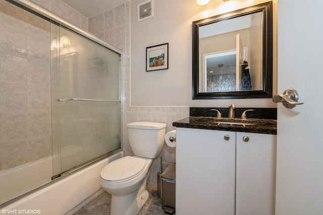 full bath with tile walls, vanity, toilet, visible vents, and enclosed tub / shower combo
