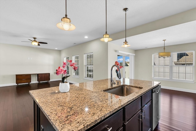 kitchen with light stone counters, a center island with sink, sink, and dark hardwood / wood-style flooring