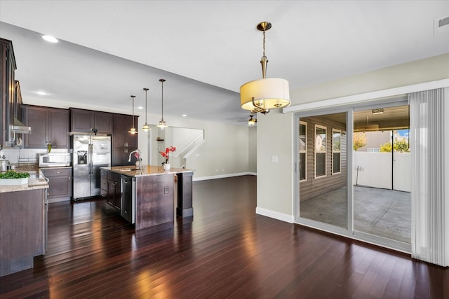 kitchen with a kitchen island with sink, dark hardwood / wood-style flooring, dark brown cabinets, hanging light fixtures, and appliances with stainless steel finishes