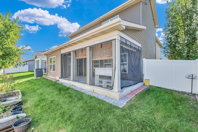 rear view of house with a sunroom, central AC unit, and a lawn