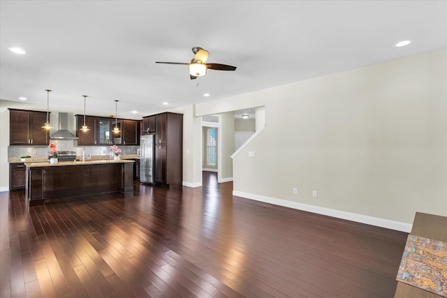 kitchen featuring a center island, stainless steel appliances, dark wood-type flooring, pendant lighting, and wall chimney range hood